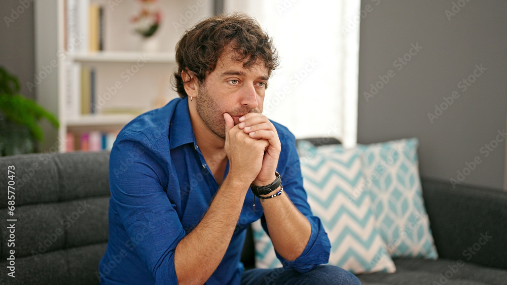 Young hispanic man sitting on sofa with serious expression at home Young hispanic man sitting on sofa with serious expression at home