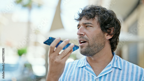 Young hispanic man sending voice message with smartphone at street