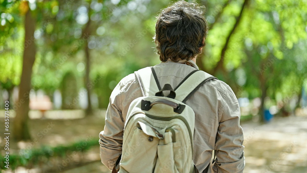 Young hispanic man tourist wearing backpack walking backwards at park