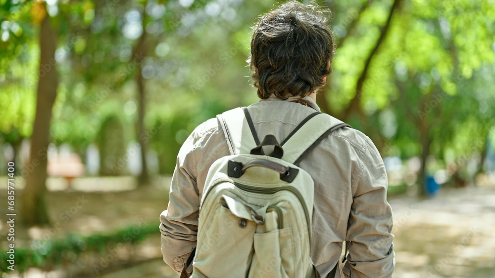 Young hispanic man tourist wearing backpack walking backwards at park Young hispanic man tourist wearing backpack walking backwards at park