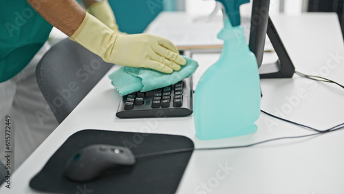 Young hispanic man cleaning keyboard with a cloth at office