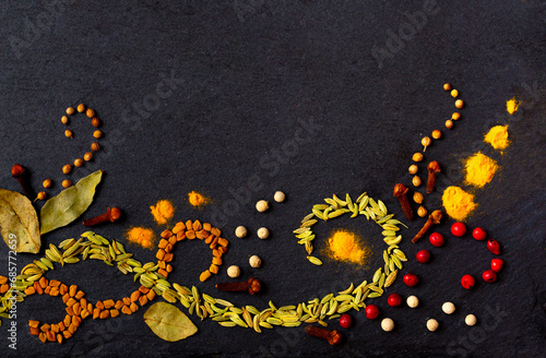Pattern of spices on a black stone table. A set of spices from India. Decoration design. Various spices, peppers and herbs close-up top view. A set of peppers and spices for cooking.