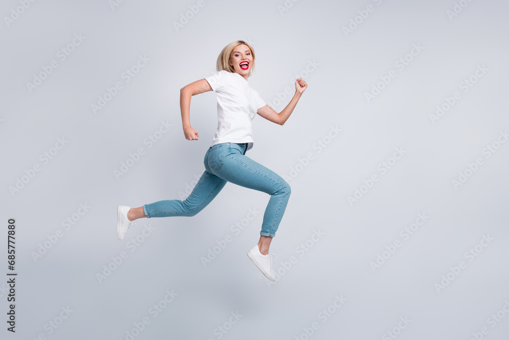 Full size photo of adorable energetic woman dressed white t-shirt denim pants run in empty space isolated on white color background