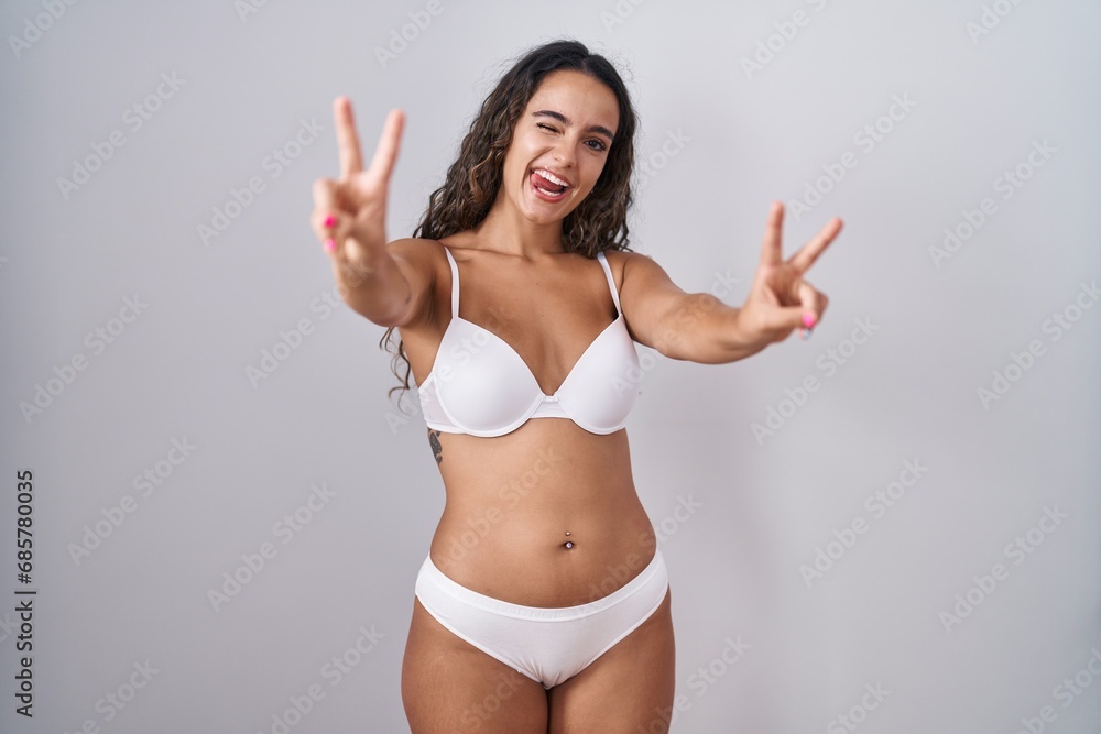 Young hispanic woman wearing white lingerie smiling with tongue out showing fingers of both hands doing victory sign. number two. Young hispanic woman wearing white lingerie smiling with tongue out showing fingers of both hands doing victory sign. number two.