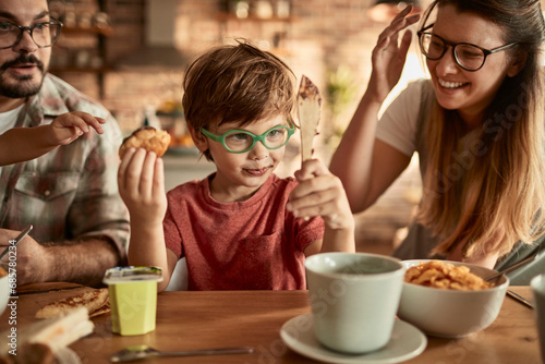 Little boy in glasses having breakfast with parents at home photo