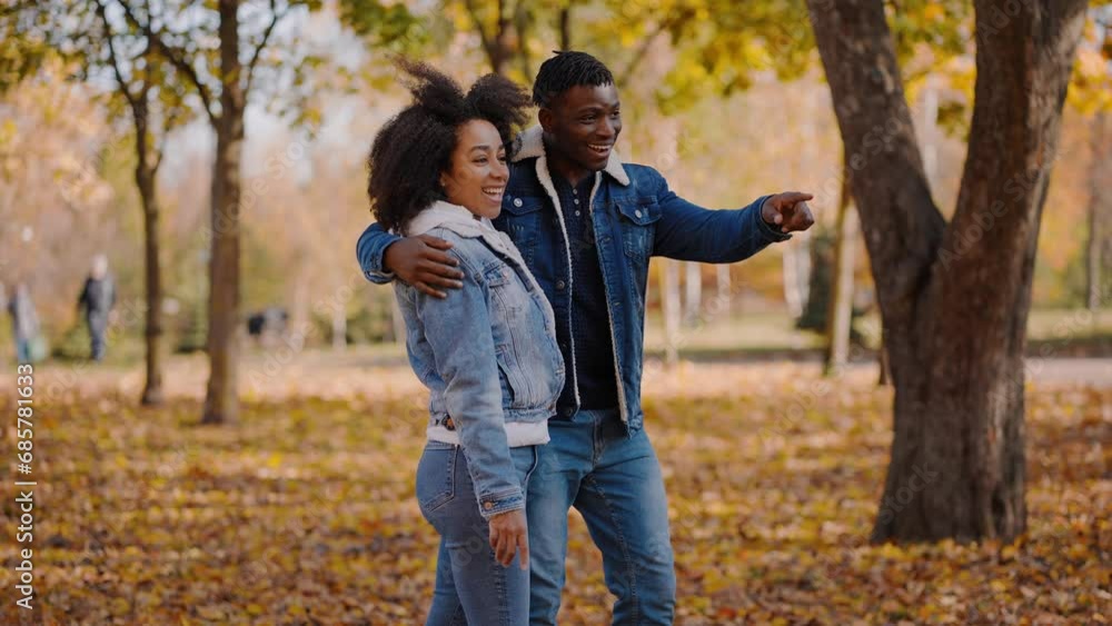 Black couple walks on day pointing to yellowed trees in distance Black couple walks on day pointing to yellowed trees in distance