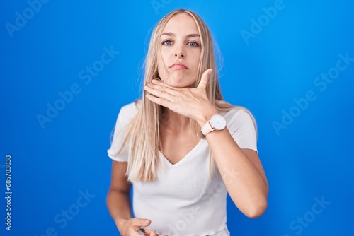 Young caucasian woman standing over blue background cutting throat with hand as knife, threaten aggression with furious violence