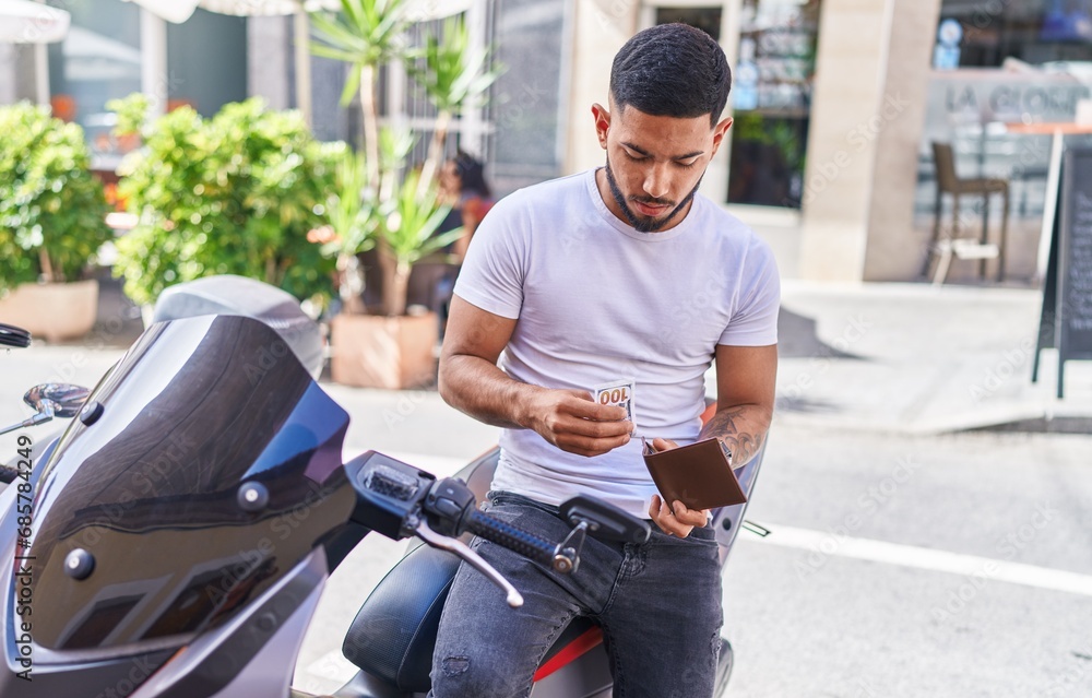 Young latin man counting dollars sitting on motorbike at street