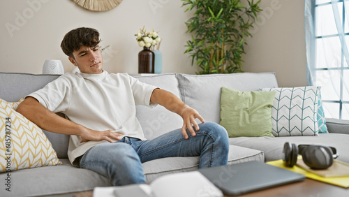 In the cozy comfort of his home, a young hispanic teenager is sitting on the sofa, a hint of doubt on his handsome face, seriously contemplating his thoughts while gazing off to the side.