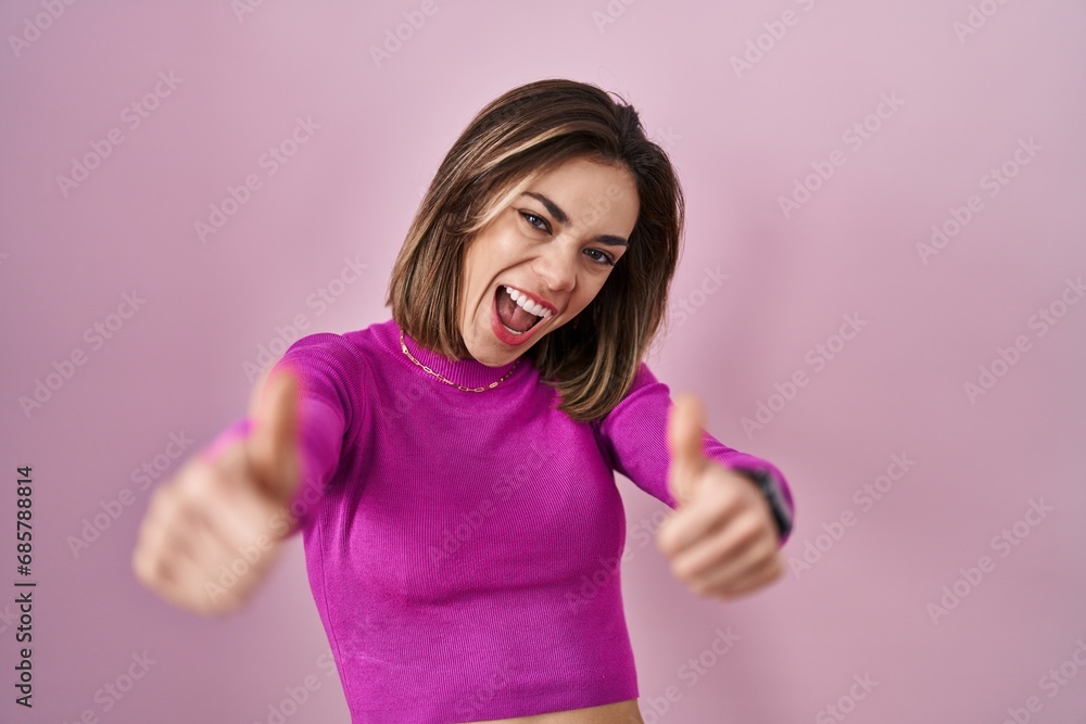 Hispanic woman standing over pink background approving doing positive gesture with hand, thumbs up smiling and happy for success. winner gesture. Hispanic woman standing over pink background approving doing positive gesture with hand, thumbs up smiling and happy for success. winner gesture.