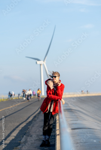 Vertical image of Caucasian waman with sunglasses stand in front of wind turbine or windmill also look to left side near the road.