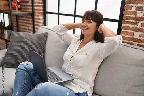Young beautiful hispanic woman using laptop relaxed on sofa at home