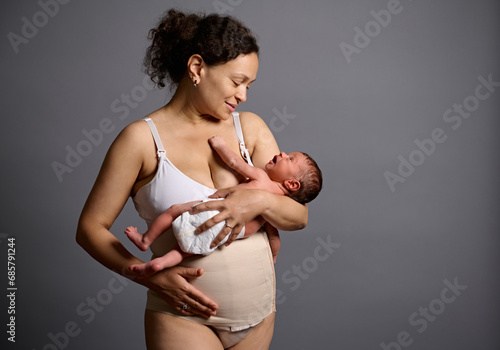 Happy mother in underwear and elastic bandage on her belly after c-section, smiling looking at her newborn baby