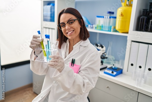Fototapeta Naklejka Na Ścianę i Meble -  Young beautiful hispanic woman scientist smiling confident holding test tubes at laboratory