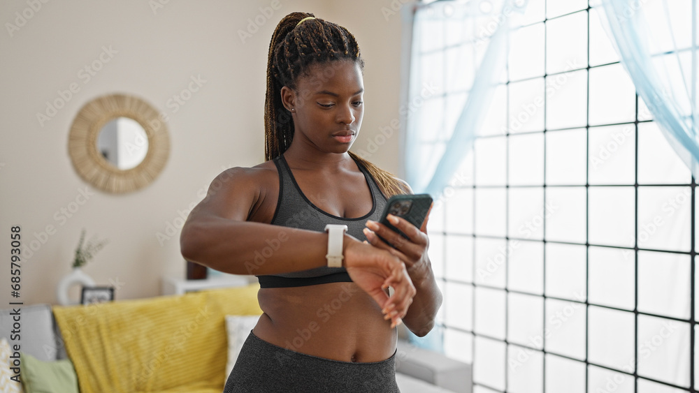 © Krakenimages.com - African american woman wearing sportswear using smartphone and watch at home