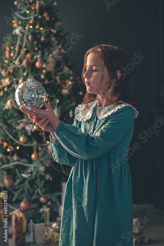 cute girl holds a disco ball against the background of a Christmas tree