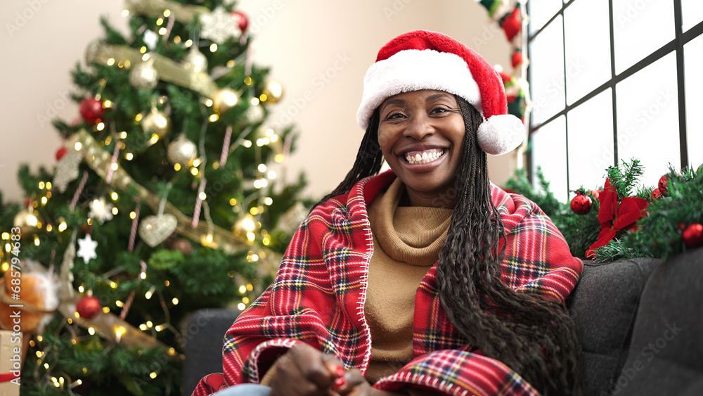 African woman smiling sitting by christmas tree at home African woman smiling sitting by christmas tree at home