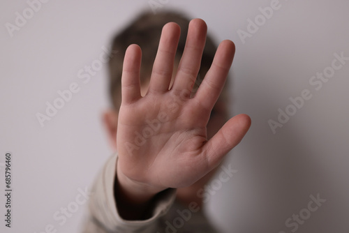Child abuse. Boy doing stop gesture on light grey background, selective focus