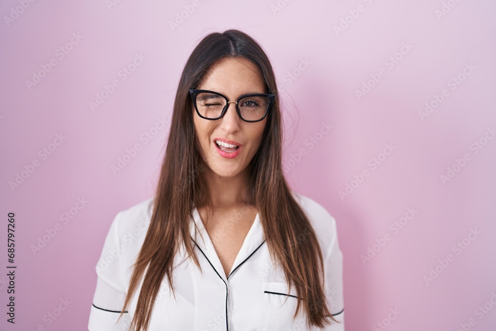 Young brunette woman wearing glasses standing over pink background winking looking at the camera with sexy expression, cheerful and happy face. Young brunette woman wearing glasses standing over pink background winking looking at the camera with sexy expression, cheerful and happy face.
