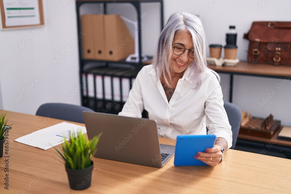 Middle age grey-haired woman business worker using touchpad and laptop at office Middle age grey-haired woman business worker using touchpad and laptop at office