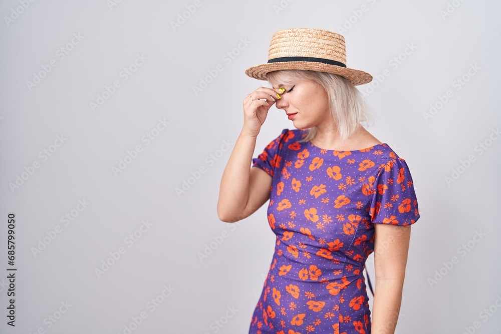 Young caucasian woman wearing flowers dress and summer hat tired rubbing nose and eyes feeling fatigue and headache. stress and frustration concept. Young caucasian woman wearing flowers dress and summer hat tired rubbing nose and eyes feeling fatigue and headache. stress and frustration concept.