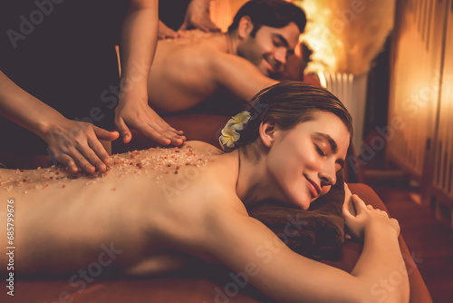 Couple customer having exfoliation treatment in luxury spa salon with warmth candle light ambient. Salt scrub beauty treatment in Health spa body scrub. Quiescent photo