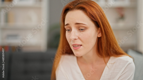 Young redhead woman sitting on sofa with serious face speaking at home