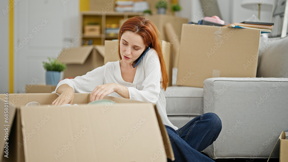 Young redhead woman unpacking cardboard box speaking on the phone at new home Young redhead woman unpacking cardboard box speaking on the phone at new home