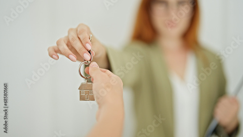 Young redhead woman real state agent giving keys to client at home