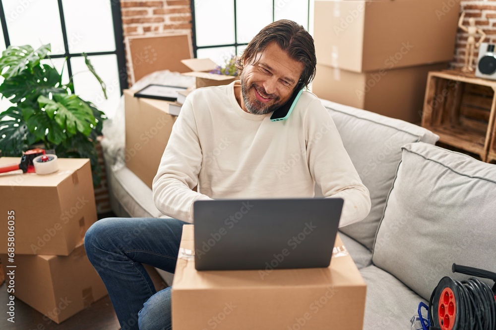 Middle age man using laptop talking on smartphone at new home Middle age man using laptop talking on smartphone at new home