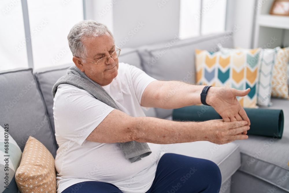 Obraz premium Middle age grey-haired man stretching arm sitting on sofa at home