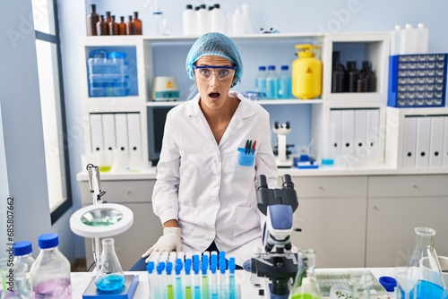 Brunette woman working at scientist laboratory afraid and shocked with surprise and amazed expression  fear and excited face.