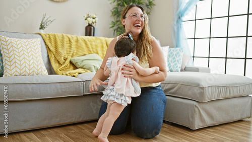 Joyous mother embracing daughter, chuckling and flashing beaming smiles in cozy home