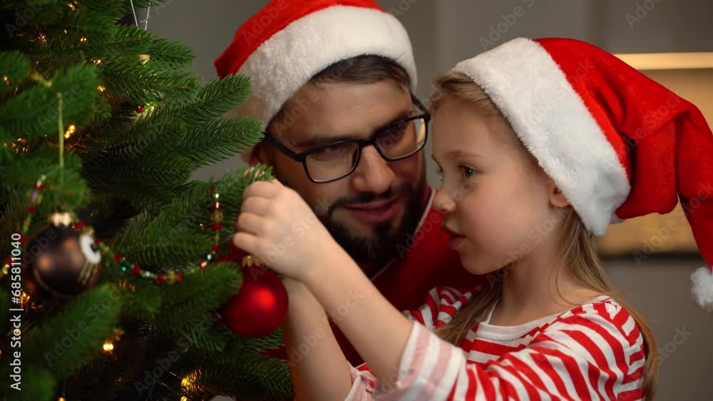 Father and daughter in red santa hats fun decorate Christmas tree with red ball at home. Happy family celebrate New Year and Christmas Father and daughter in red santa hats fun decorate Christmas tree with red ball at home. Happy family celebrate New Year and Christmas