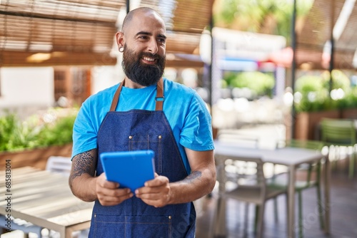 Young bald man waiter smiling confident using touchpad at coffee shop terrace