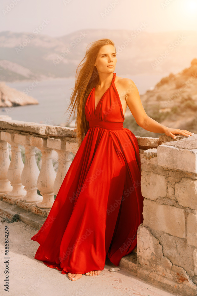 Woman red dress. Summer lifestyle of a happy woman posing near a fence with balusters over the sea.