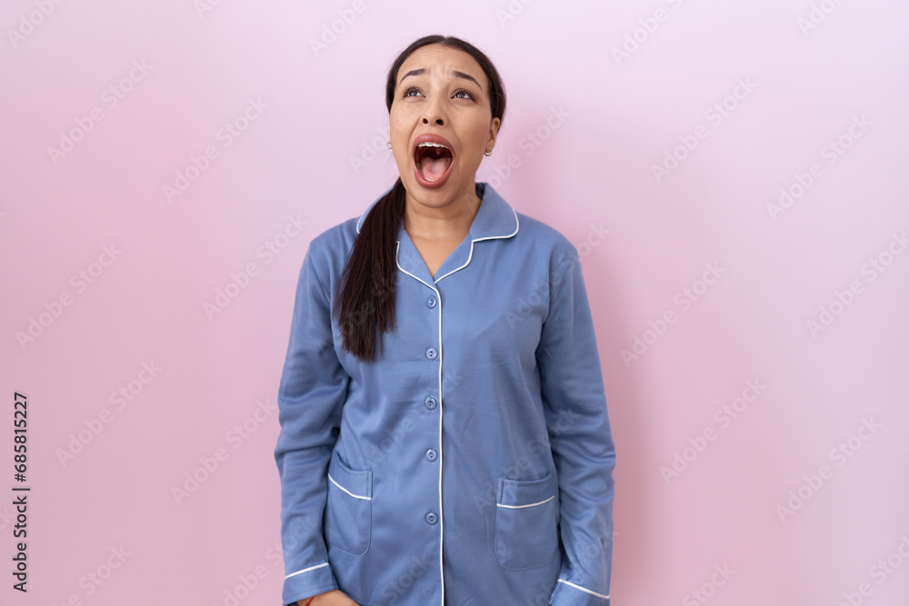 Young arab woman wearing blue pajama angry and mad screaming frustrated and furious, shouting with anger. rage and aggressive concept. Young arab woman wearing blue pajama angry and mad screaming frustrated and furious, shouting with anger. rage and aggressive concept.