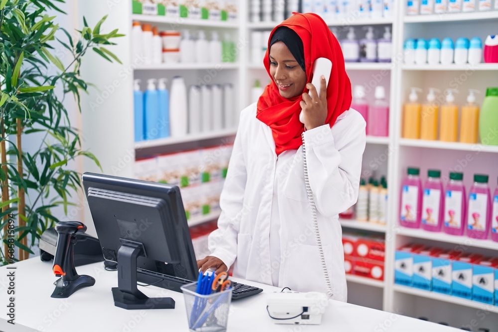 Young beautiful woman pharmacist talking on telephone using computer at pharmacy Young beautiful woman pharmacist talking on telephone using computer at pharmacy
