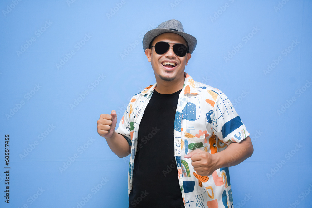 Overjoyed asian man wearing sunglasses dancing, smiles positively, being in high spirit. isolated on blue background. holiday and vacation concept Overjoyed asian man wearing sunglasses dancing, smiles positively, being in high spirit. isolated on blue background. holiday and vacation concept