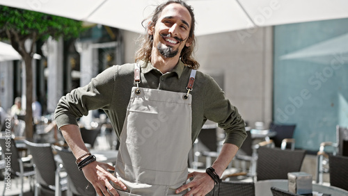 Young hispanic man waiter smiling confident standing at coffee shop terrace