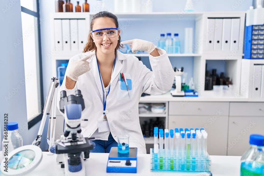 Fototapeta premium Young hispanic woman working at scientist laboratory smiling cheerful showing and pointing with fingers teeth and mouth. dental health concept.