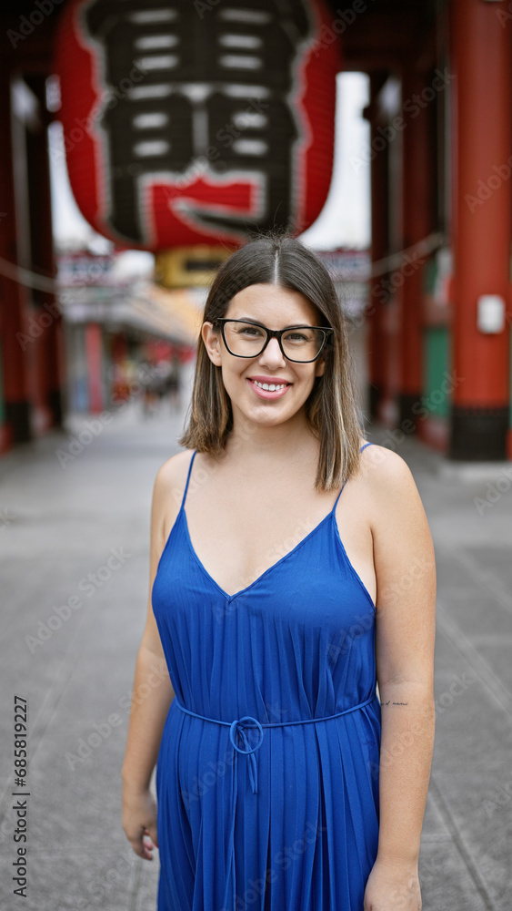 Beautiful hispanic woman donning glasses, flashing a cheerful smile at the senso-ji temple, immersed in japanese tradition, joyful latin adult exploring the rich culture of tokyo