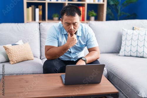 Young chinese man using laptop with serious expression at home