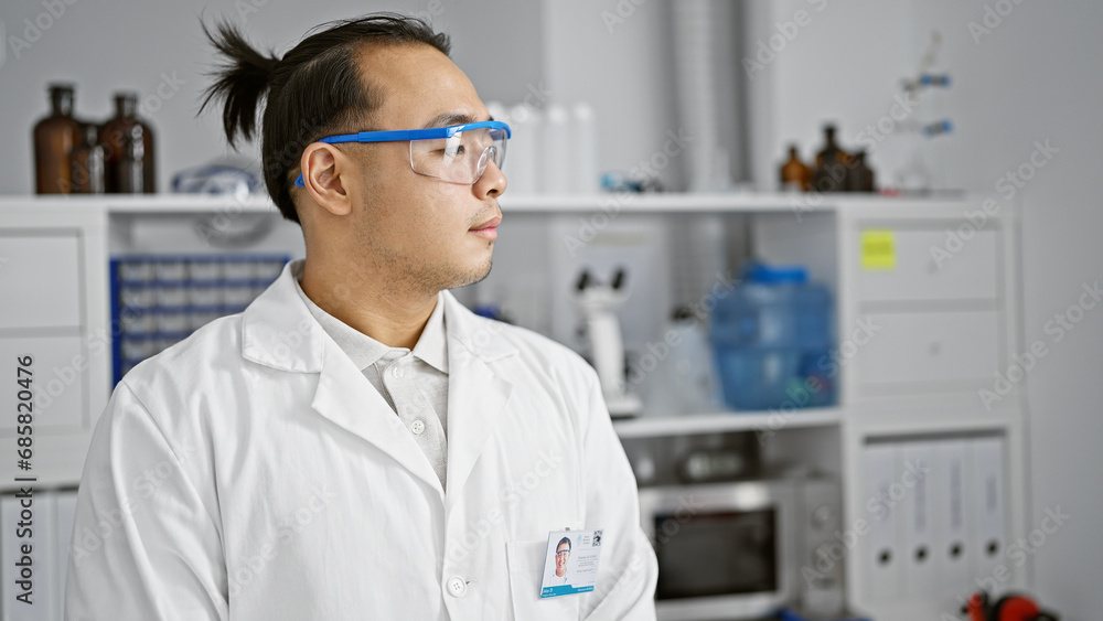 Serious young chinese man, a lab scientist in safety glasses, deep in concentration on medical research at a bustling, professional chemistry lab. Serious young chinese man, a lab scientist in safety glasses, deep in concentration on medical research at a bustling, professional chemistry lab.