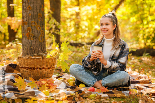 A young girl in the autumn forest drinks coffee with a plaid plaid, a beautiful autumn atmosphere
