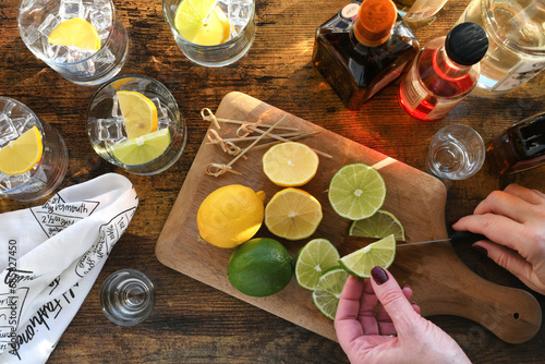 Female preparing cocktails with liquor alcohol lemons limes on a wooden bar - high angle overhead view flat lay