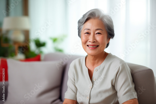 a Smiling asianwoman sitting on sofa at home, single mature senior in living room