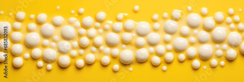 Close-up of dripping white liquid drops on yellow background.