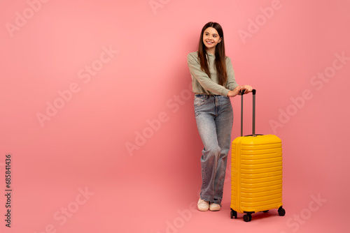 Happy teenage girl standing with bright yellow suitcase, ready for travel