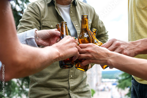 Group of people cheers with unopened beer bottles in an outdoor setting, celebrating together.